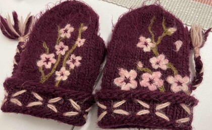 Ett par vinröda stickade tumvantar med rosa blommor och dekorativa broderier