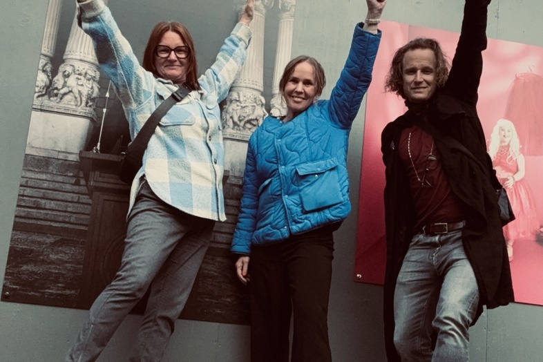 Angela Karlsson, Anna Sellén, Richard Forsberg står framför affischer och poserar med ena armen uppsträckt, leende mot kameran.