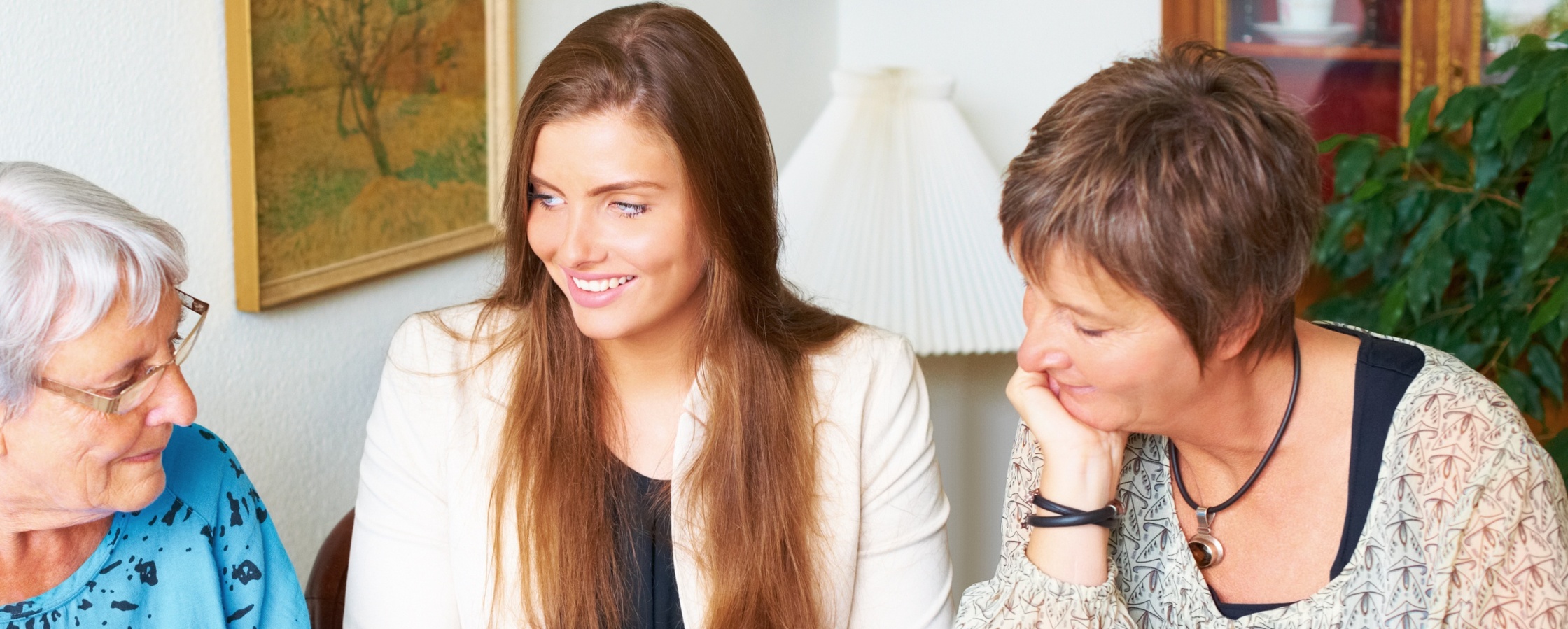 Tre personer sitter vid ett bord och tittar i ett fotoalbum med kaffe och kakor framför sig.