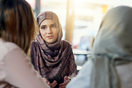 En kvinna i hijab samtalar med två andra kvinnor i ett ljust café.