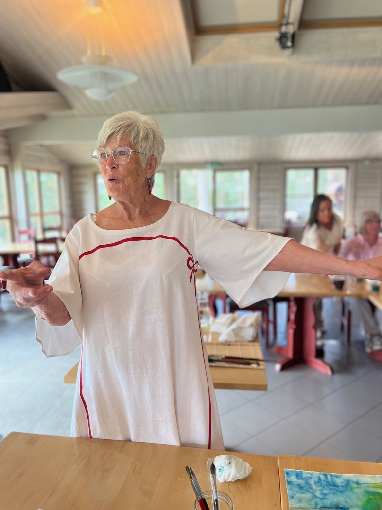 Lena Söderlund står och gestikulerar i ett ljust rum med flera personer i bakgrunden.