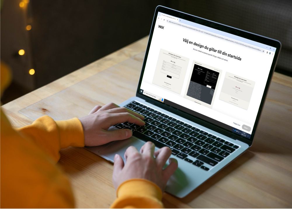 Person i gul tröja använder en bärbar dator på ett träbord, skärmen visar en webbsida om designval.