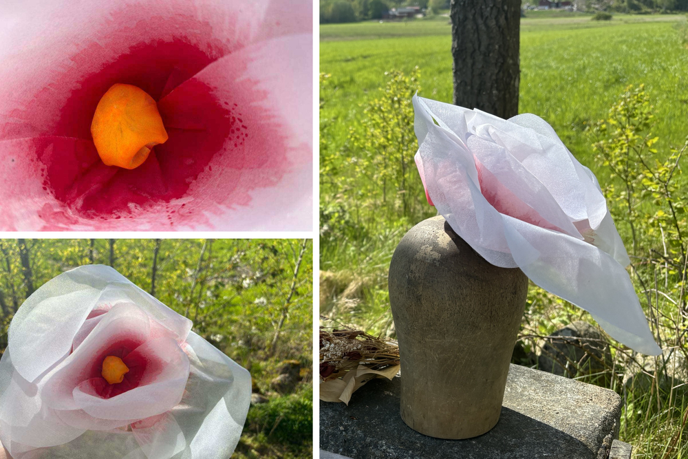 En konstgjord blomma av papper i vitt och rosa står i en vas utomhus, med närbild på blomman.