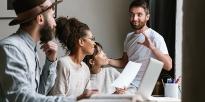Fyra personer har ett möte vid ett bord, en man står och pratar medan de andra lyssnar.