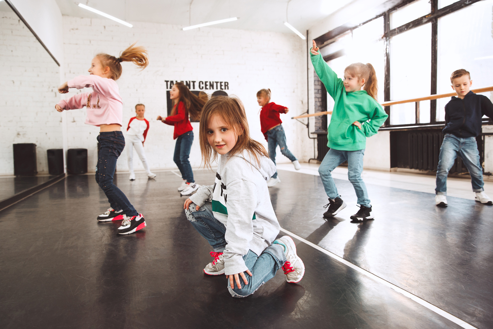 Barn dansar i en ljus dansstudio med stora fönster och spegelvägg.