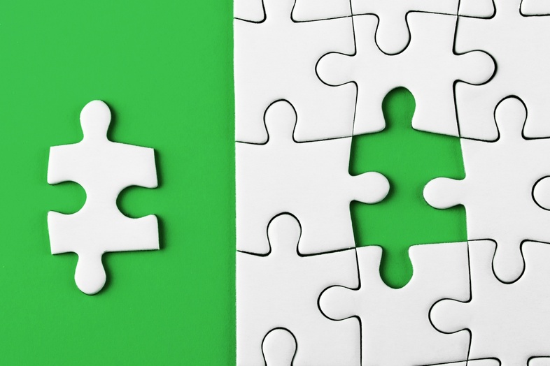 En pusselbit ligger bredvid ett pussel med en tom plats på en grön bakgrund.