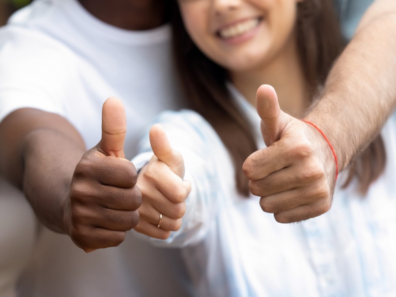 Tre personer visar tummen upp och ler, fokus på händerna och glada ansikten i bakgrunden.