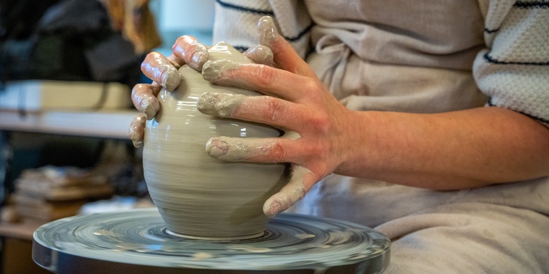 En person formar lera på en drejskiva i en keramikverkstad.