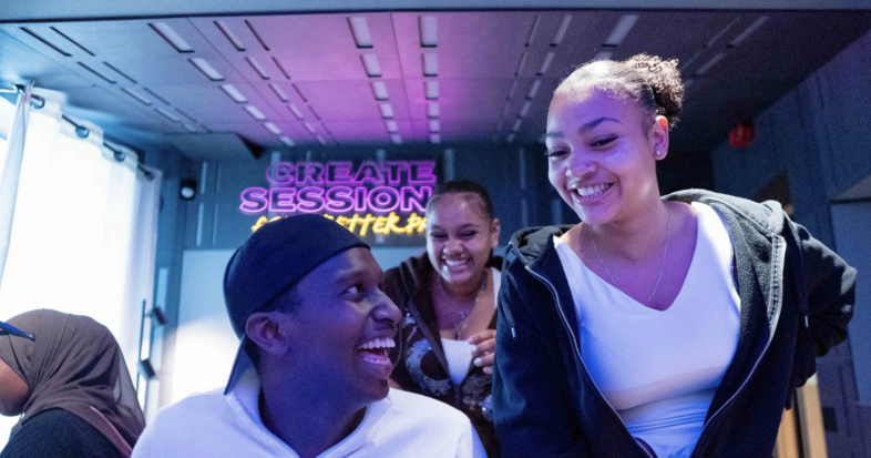 Flera personer sitter och står i ett modernt rum med neontexten 'CREATE SESSION' på väggen.