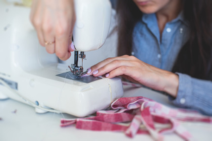 En person syr tyg med en symaskin, händerna syns tydligt vid arbetet.