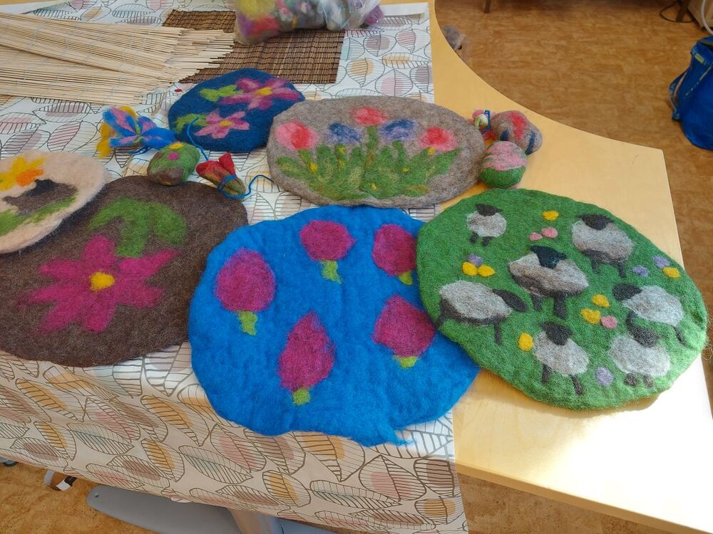 Färgglada tovade ullplattor med blommor och fårmotiv ligger på ett bord.