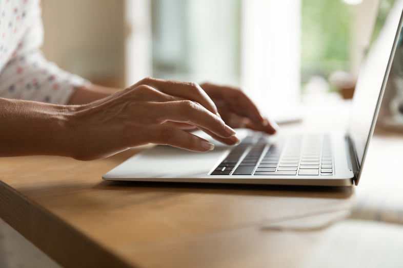 Närbild av händer som skriver på en bärbar dator vid ett träbord i ett ljust rum.