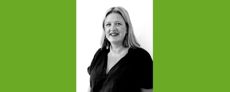 Kvinna med axellångt hår och mörk tröja ler mot kameran, svartvit bild med grön bakgrund.