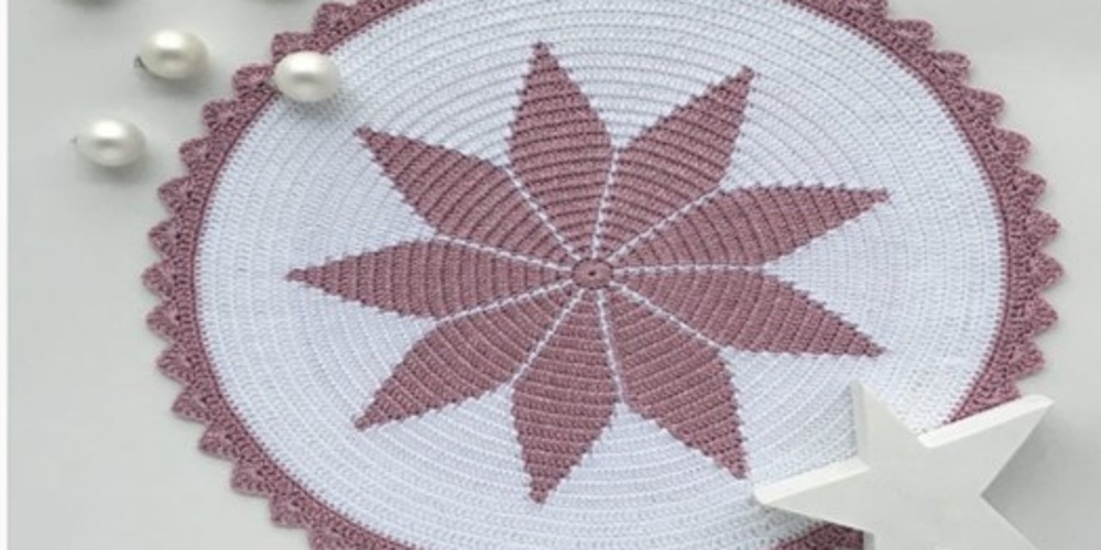Rund virkad duk med stjärnmönster i lila och vitt, dekorerad med pärlor och en vit stjärnformad prydnad.