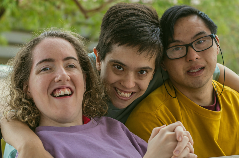 Tre personer sitter nära varandra utomhus, två håller varandra i handen.