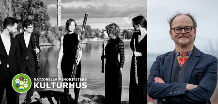 En grupp musiker med blåsinstrument står vid vattnet, och en man med glasögon och folkdräkt står bredvid.