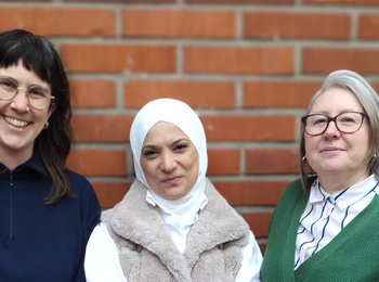 Tre personer står framför en tegelvägg utomhus, klädda i vardagskläder.
