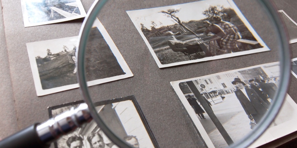 Ett fotoalbum med gamla svartvita fotografier och ett förstoringsglas ovanpå.
