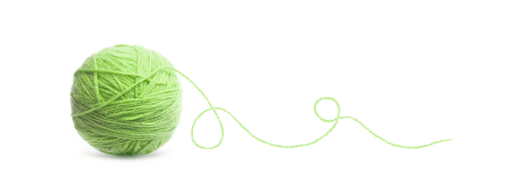 Ett nystan av ljusgrönt garn med en lös tråd på vit bakgrund.