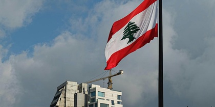 Libanons flagga vajar framför moderna och äldre byggnader under en molnig himmel.