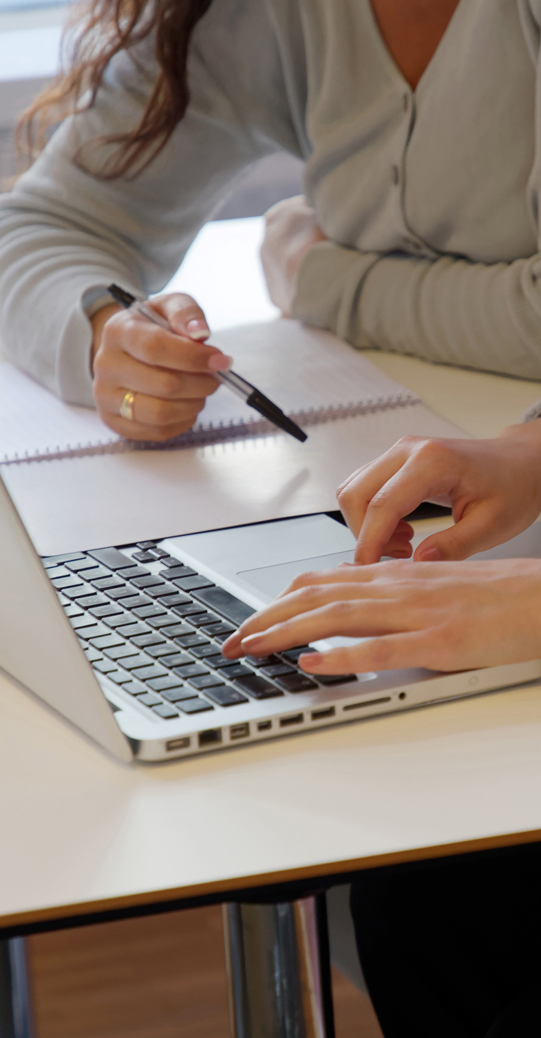 Två personer arbetar tillsammans vid ett bord med en bärbar dator och anteckningsblock.