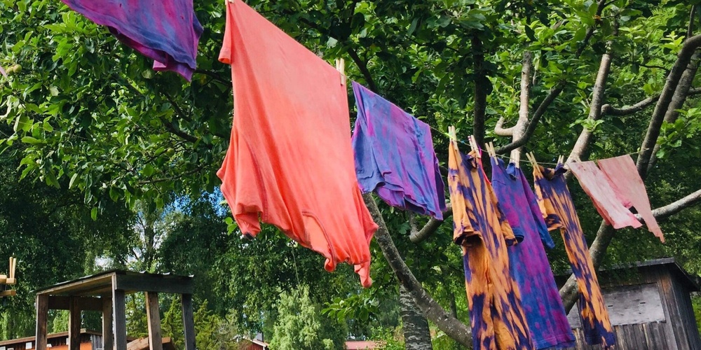 Färgglada kläder hänger på en tvättlina mellan träd i en grönskande trädgård.