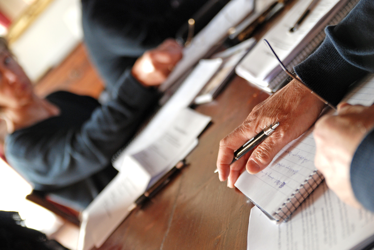Flera personer sitter vid ett bord och skriver i anteckningsblock med papper och pennor.
